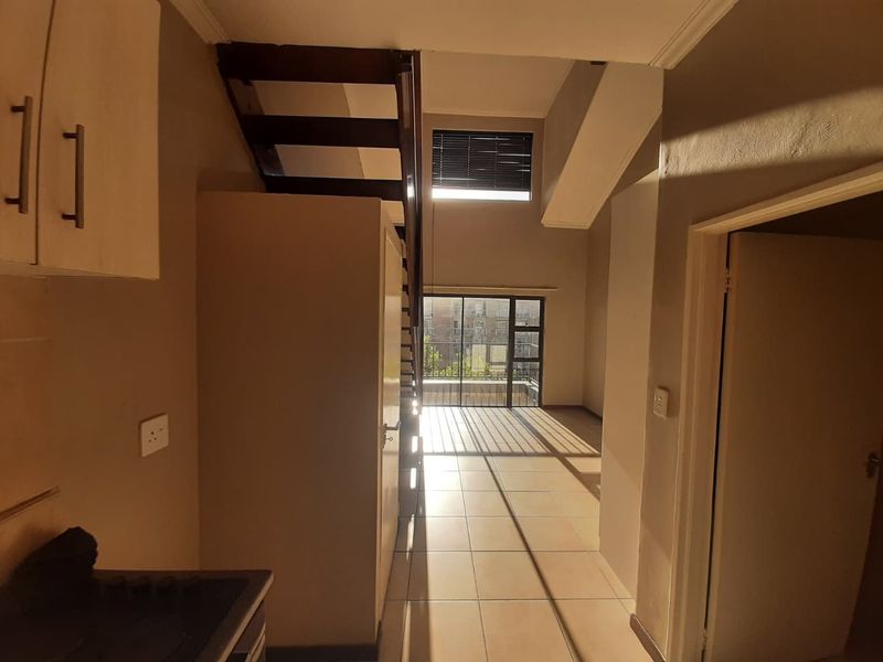 Open plan living area featuring tiled flooring, a staircase leading to an upper level, and a sliding glass door providing natural light.
