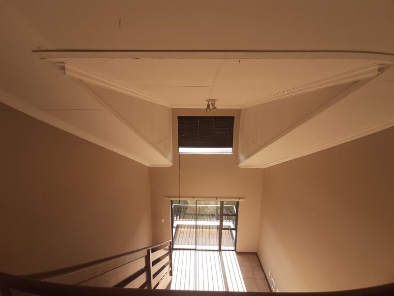 A high-ceilinged hallway featuring a skylight, tiled flooring, and a sliding glass door leading to an outdoor area, viewed from the upper level.