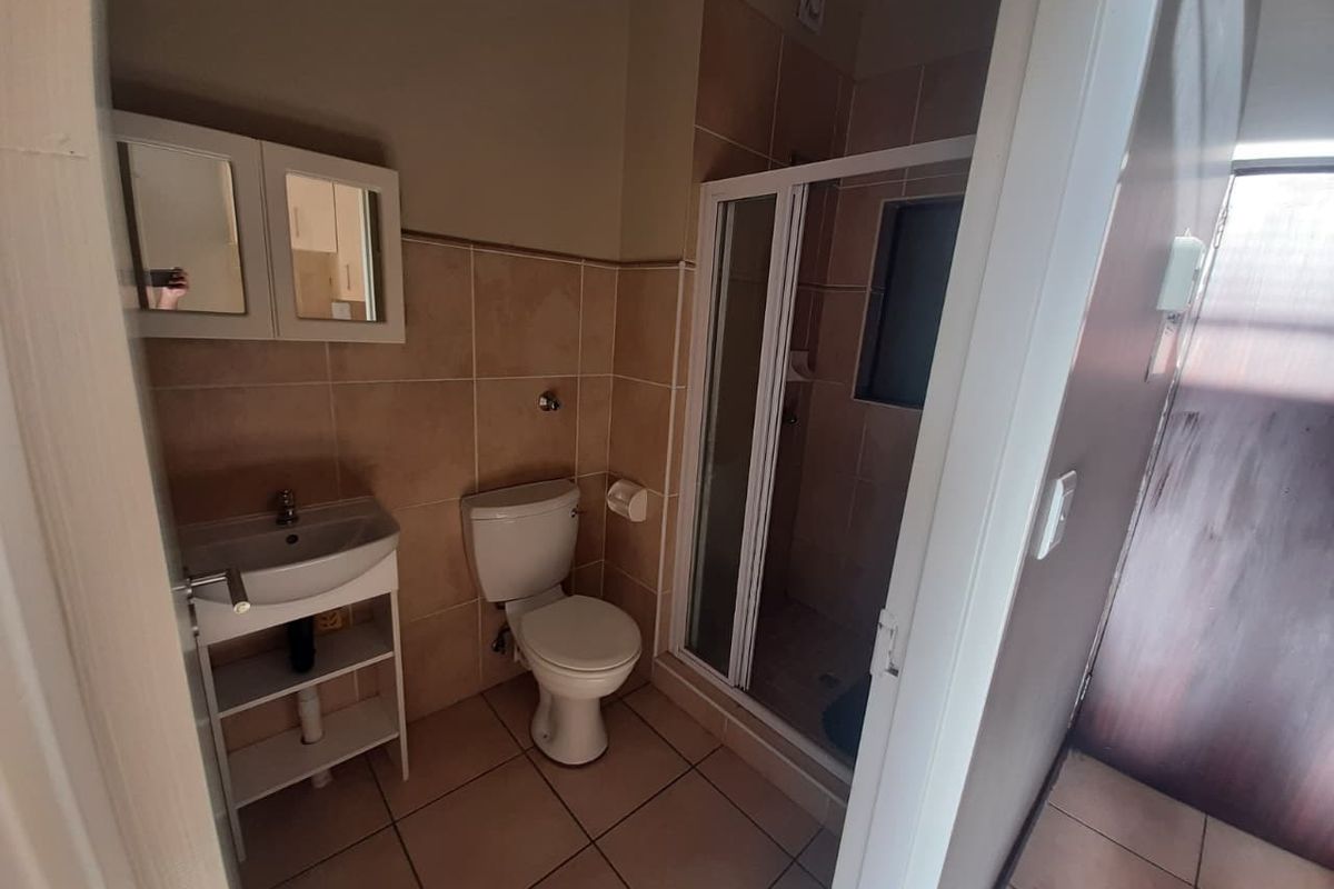 A functional bathroom featuring tiled walls and floors, a shower enclosure, a pedestal basin, and a toilet.