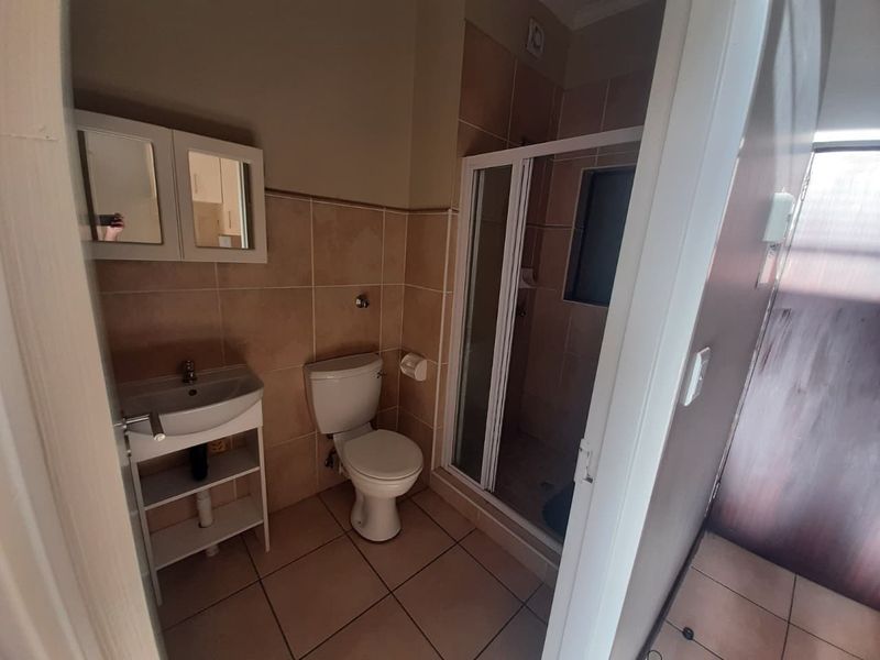 A functional bathroom featuring tiled walls and floors, a shower enclosure, a pedestal basin, and a toilet.