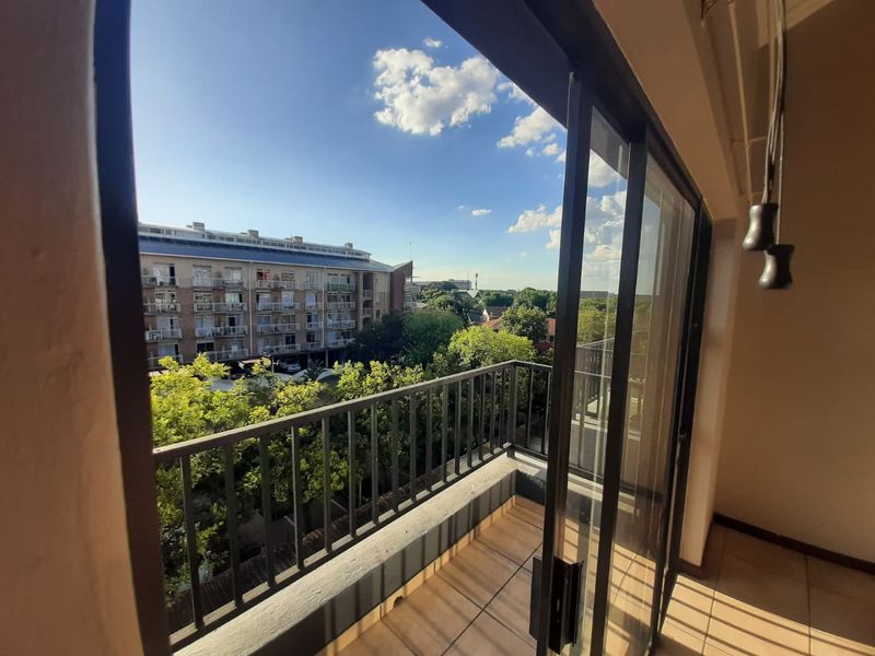 A private balcony featuring tiled flooring, a metal balustrade, and sliding glass doors, offering an elevated view of the surrounding neighborhood and trees.