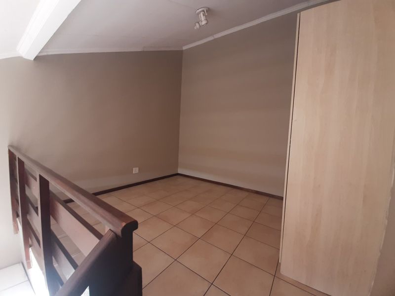 An empty bedroom featuring tiled flooring, a built-in wardrobe, and a wooden balustrade overlooking the lower level.