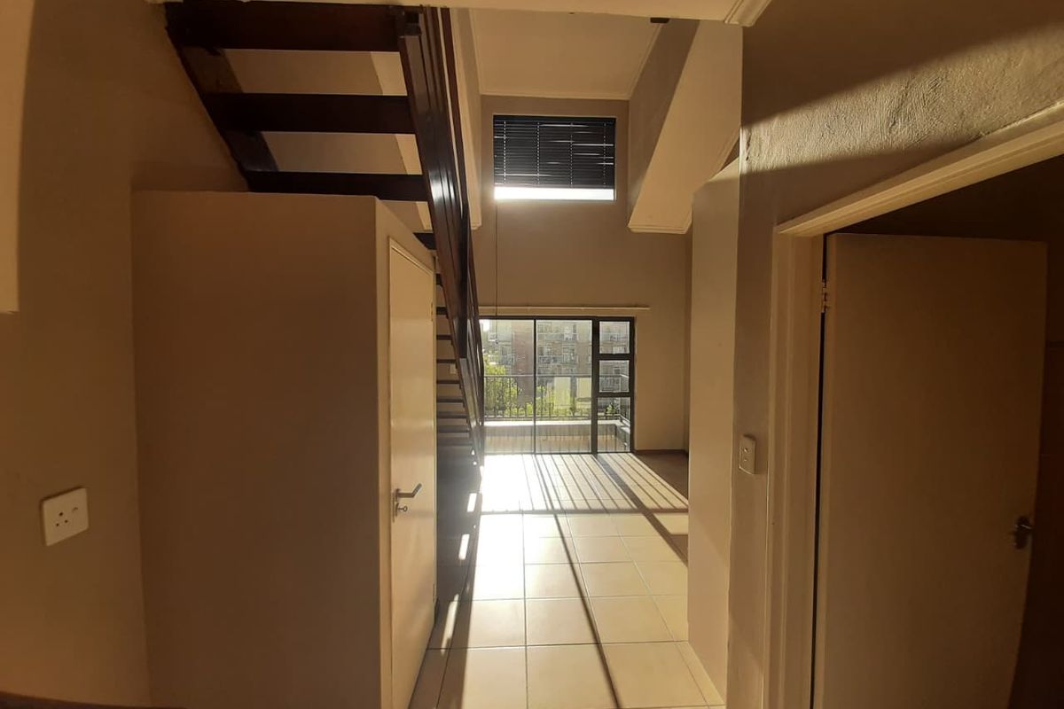 Spacious open-plan living area featuring a wooden staircase, tiled flooring, and large sliding glass doors that provide ample natural light.