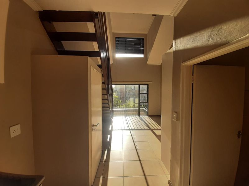 Spacious open-plan living area featuring a wooden staircase, tiled flooring, and large sliding glass doors that provide ample natural light.