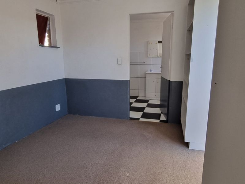 A vacant bedroom featuring built-in storage and direct access to an en-suite bathroom with a classic checkerboard floor finish.