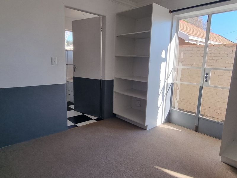 A bedroom featuring built-in shelving, a wardrobe, and a sliding glass door leading to an outdoor area, with an adjoining bathroom.