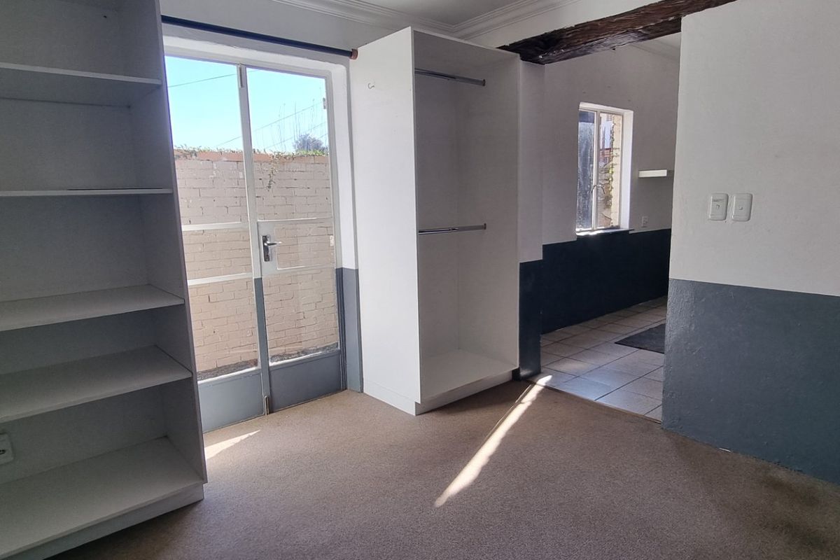 An empty bedroom featuring built-in storage, an exposed timber beam, and direct access to an outdoor area through a glass door.