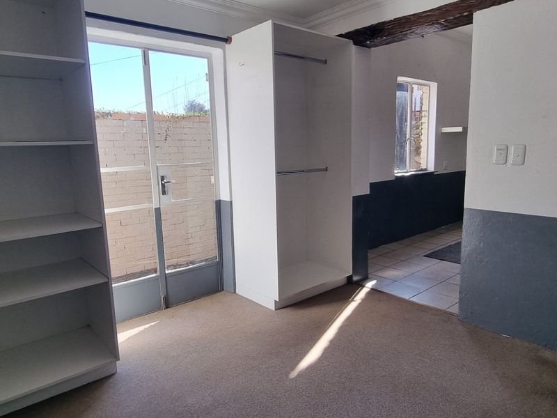 An empty bedroom featuring built-in storage, an exposed timber beam, and direct access to an outdoor area through a glass door.