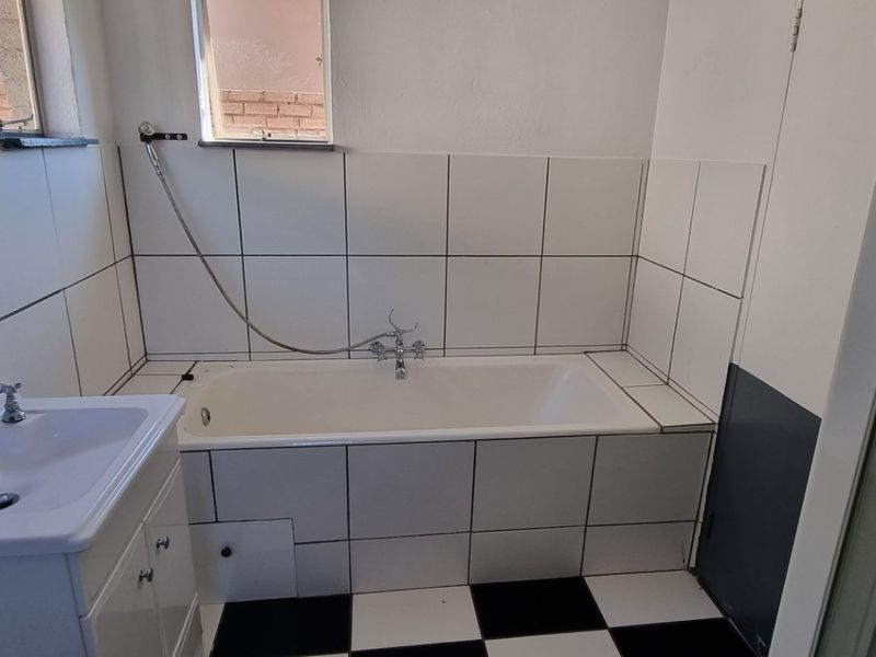 A functional bathroom featuring a bathtub, vanity basin, and separate shower enclosure with classic black and white tiled flooring.