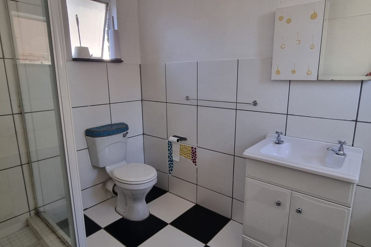 A functional bathroom featuring a shower enclosure, a vanity basin, and a classic black and white tiled floor.