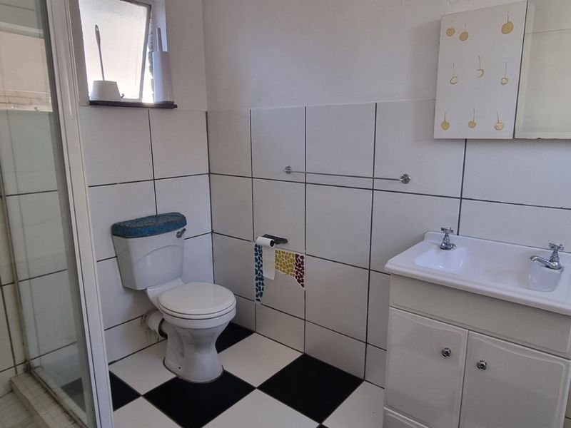 A functional bathroom featuring a shower enclosure, a vanity basin, and a classic black and white tiled floor.
