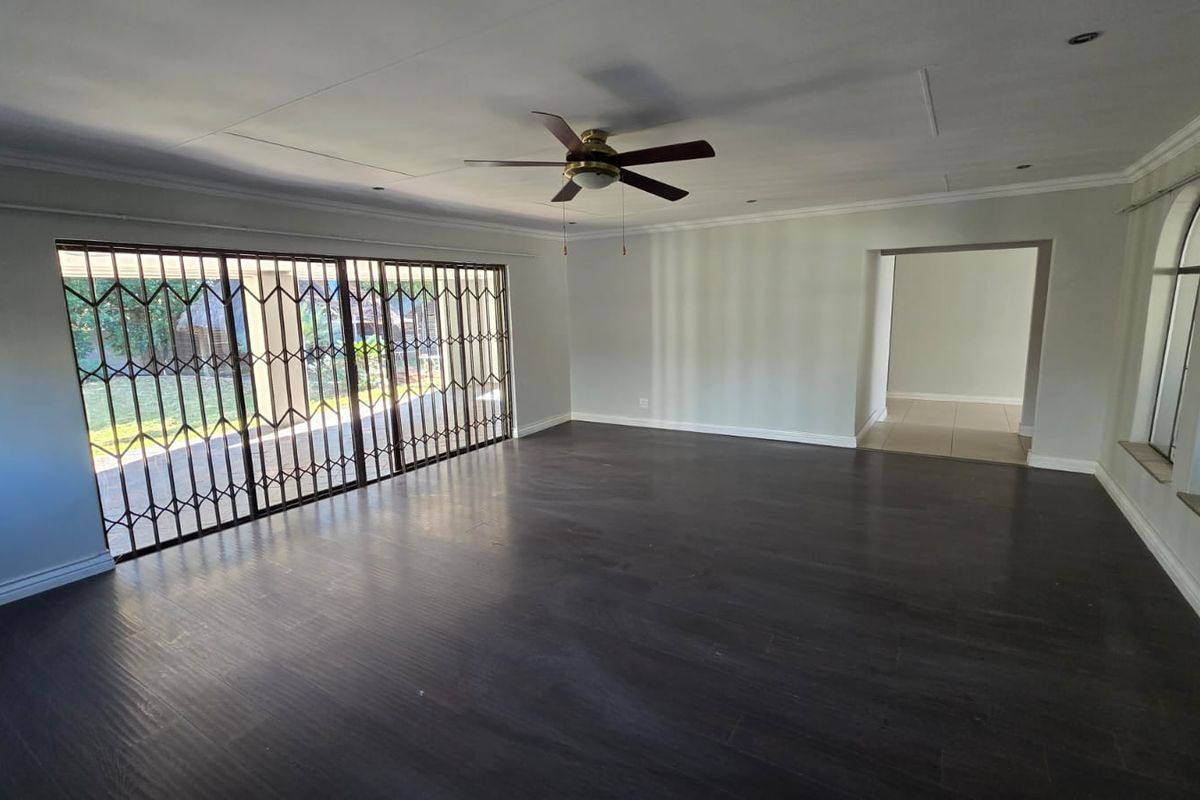Spacious, empty living room featuring dark laminate flooring, a ceiling fan, and large sliding glass doors with security gates leading to the patio.