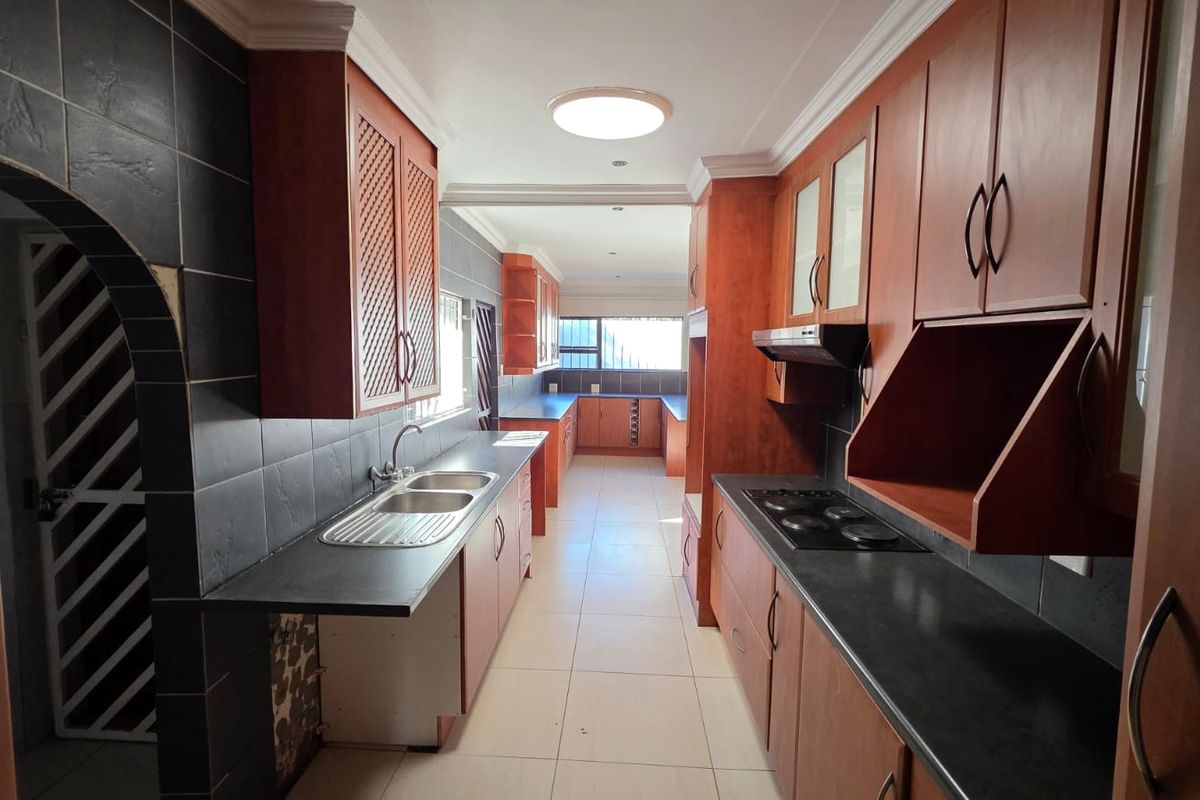 A spacious galley-style kitchen featuring wooden cabinetry, dark tiled splashbacks, a double bowl sink, and a built-in electric hob with an extractor fan.