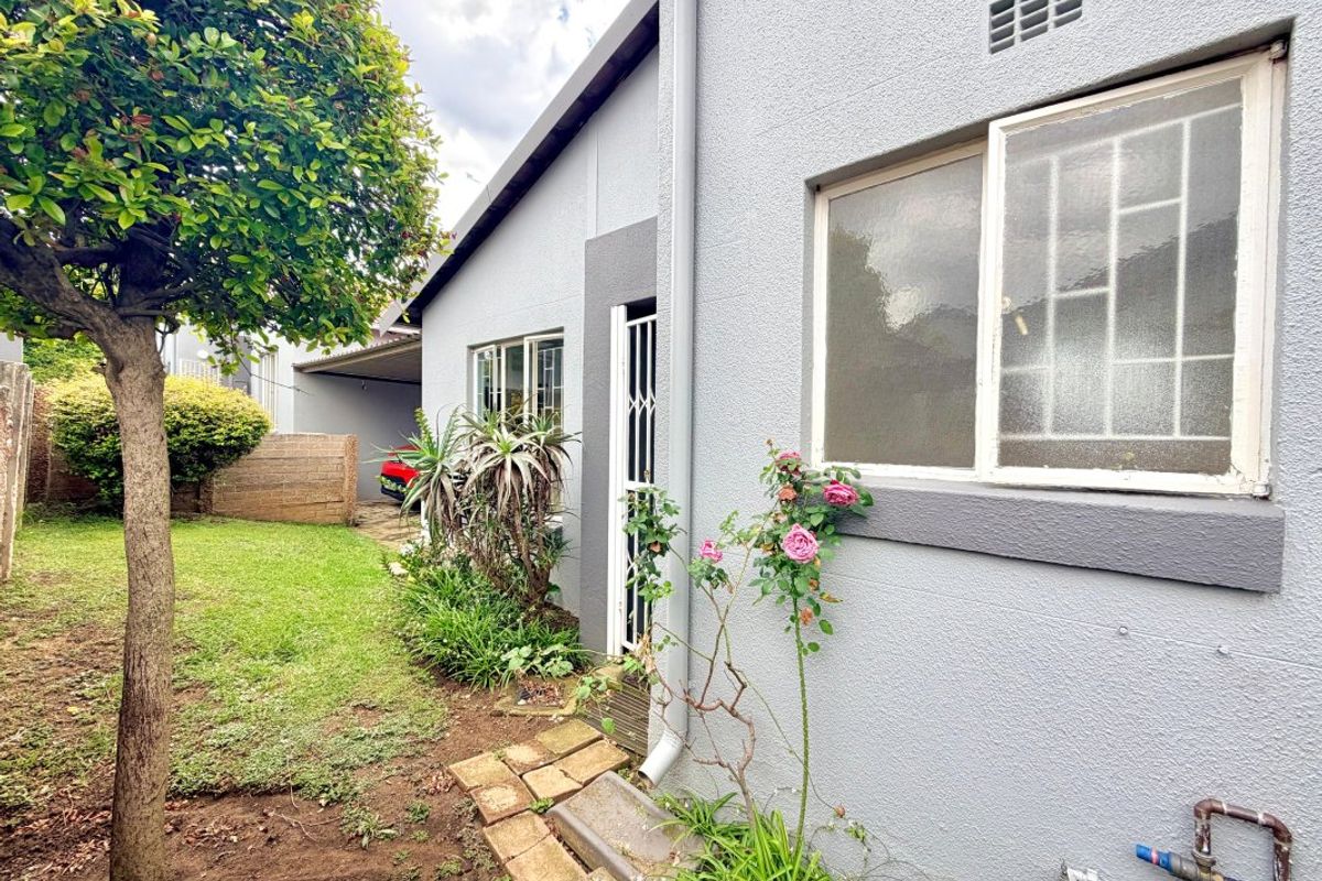 Rear exterior view of the apartment featuring a small garden area, security gate, and window security bars.