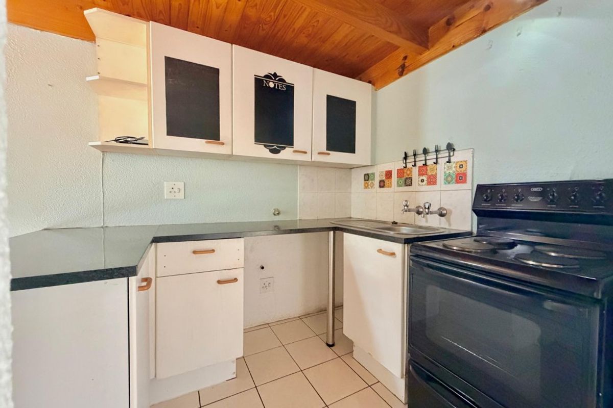 Compact kitchen featuring timber ceiling, tiled flooring, built-in cabinetry, and a freestanding stove, offering potential for modernization and improved layout efficiency.