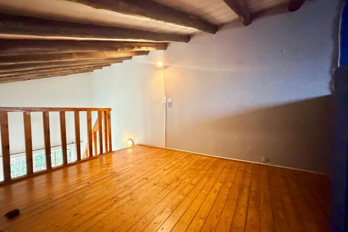 An empty loft-style bedroom featuring exposed timber ceiling beams, polished timber flooring, and a wooden balustrade overlooking the lower level.