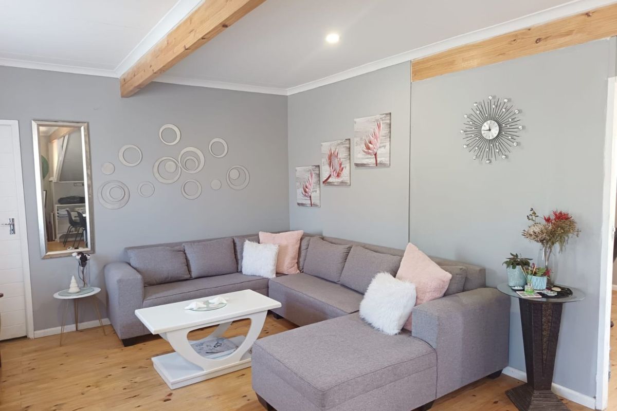 A well-maintained living room featuring exposed timber ceiling beams, polished timber flooring, and neutral grey wall finishes.