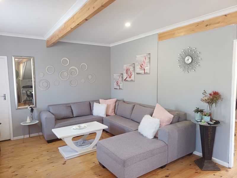 A well-maintained living room featuring exposed timber ceiling beams, polished timber flooring, and neutral grey wall finishes.