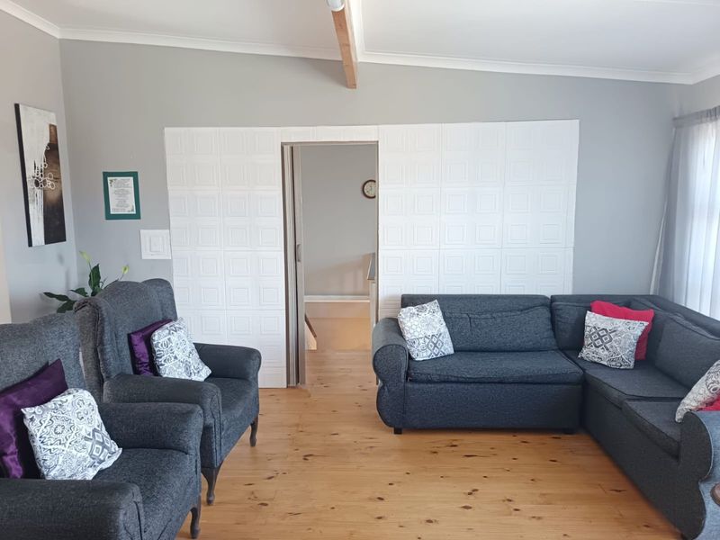 A living room featuring timber flooring, an exposed ceiling beam, and decorative wall paneling surrounding the doorway.