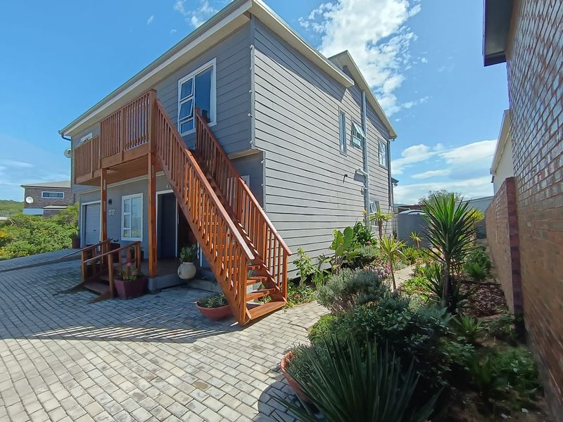 Front exterior view of a two-story house featuring timber staircase access to the upper level, paved driveway, and landscaped garden area.