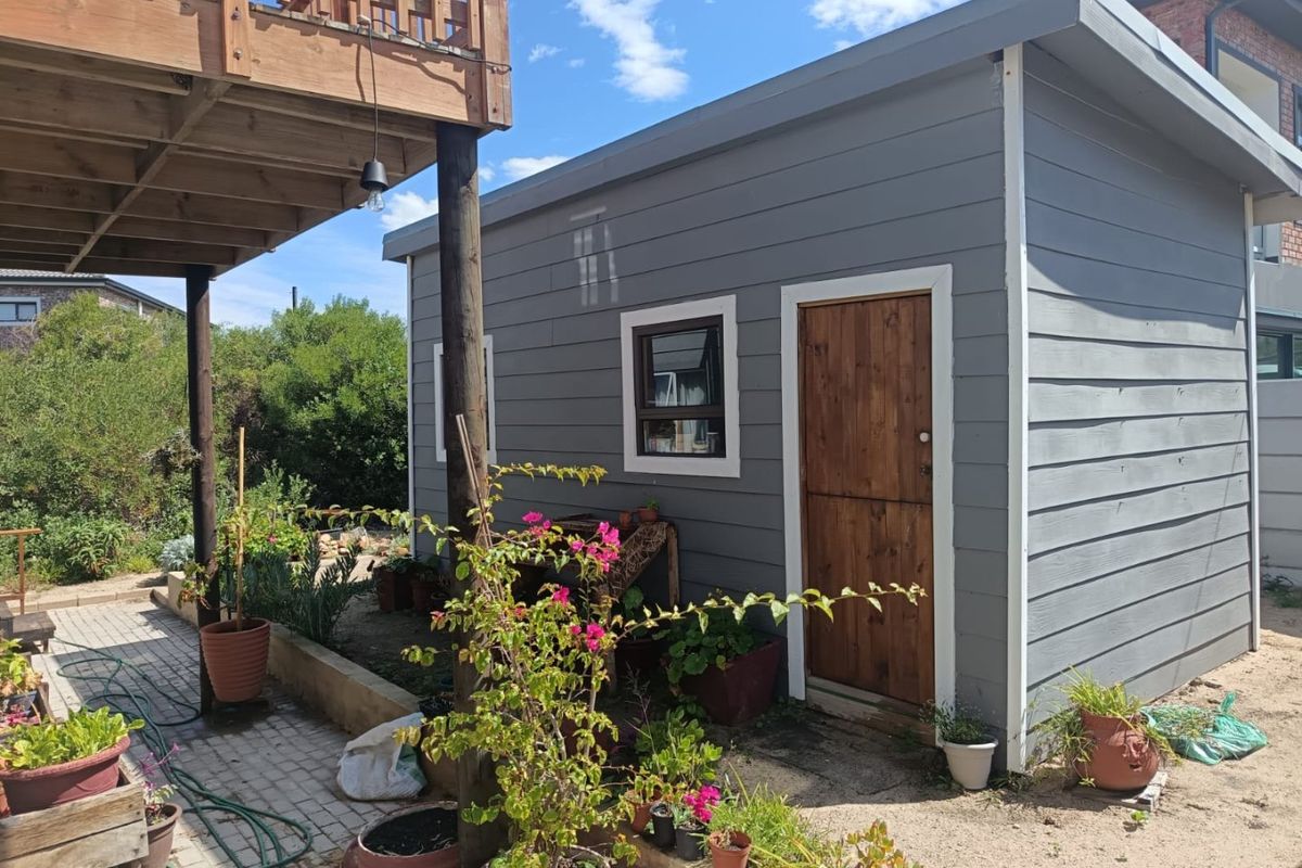 A rear view of the property featuring a timber-clad outbuilding, a raised timber deck, and a paved patio area in a garden setting.