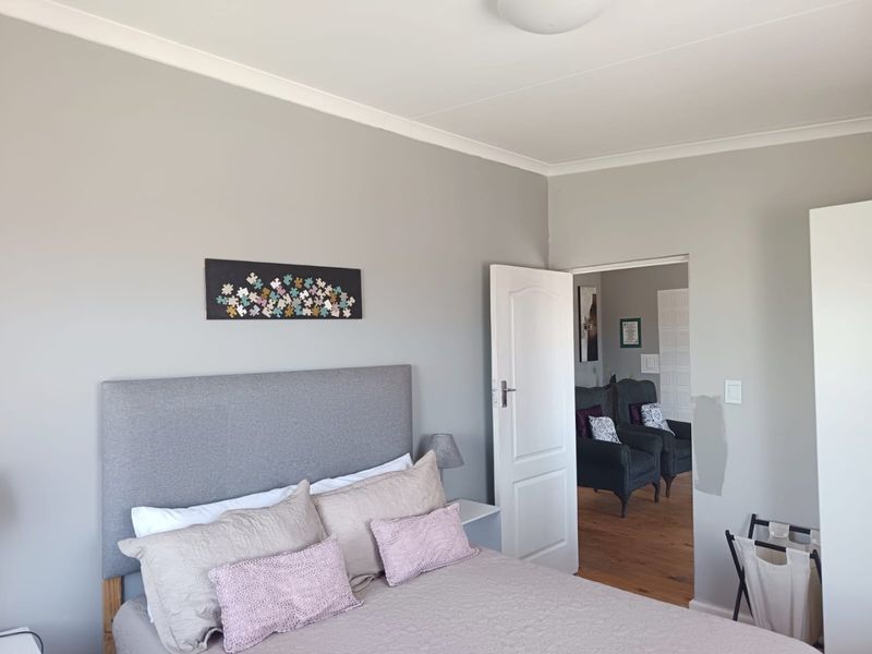 A bedroom featuring neutral grey walls, cove cornicing, and a panelled interior door leading to an adjacent living space.