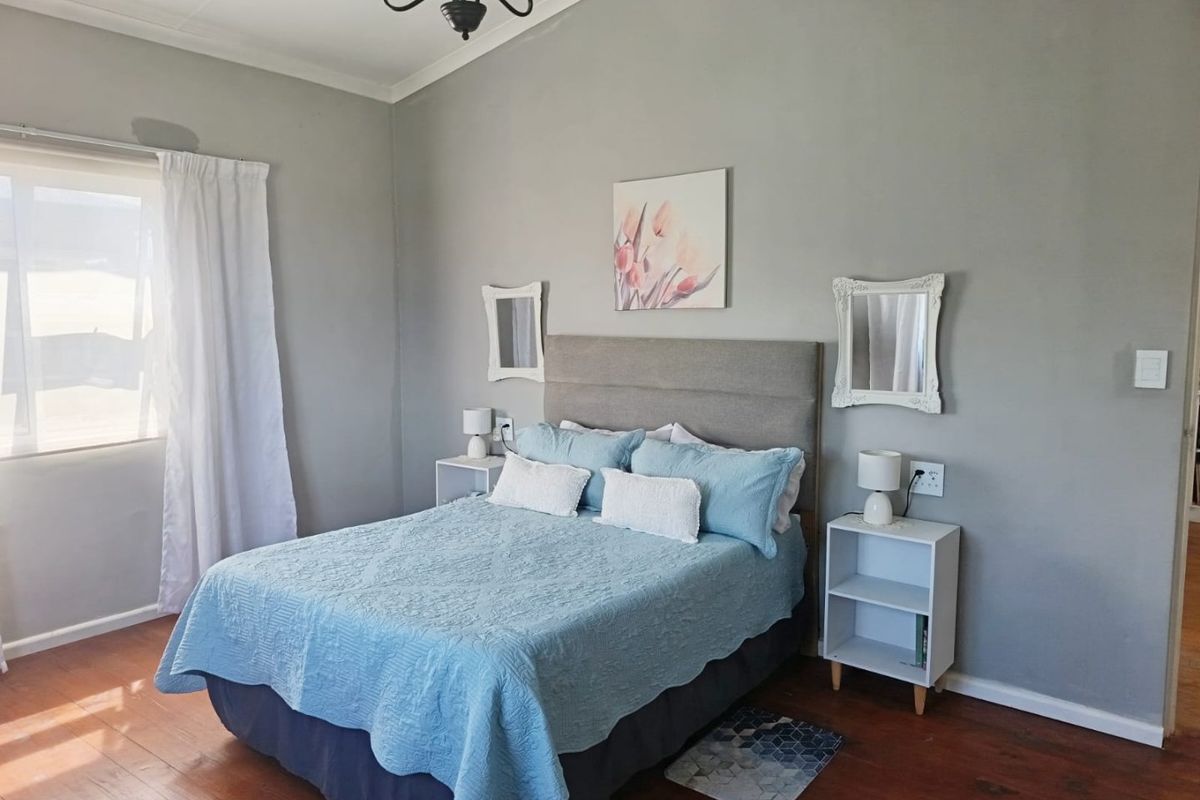 A bedroom featuring timber flooring and a coved ceiling, with a visible damp patch on the wall above the window.