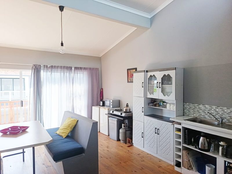 Open plan living and kitchen area featuring timber flooring, vaulted ceilings, and functional built-in cabinetry with a mosaic tile backsplash.