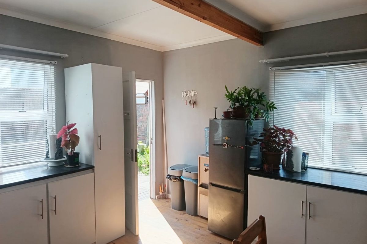 A functional kitchen area featuring white cabinetry, dark countertops, exposed timber ceiling beams, and direct access to the rear exterior.