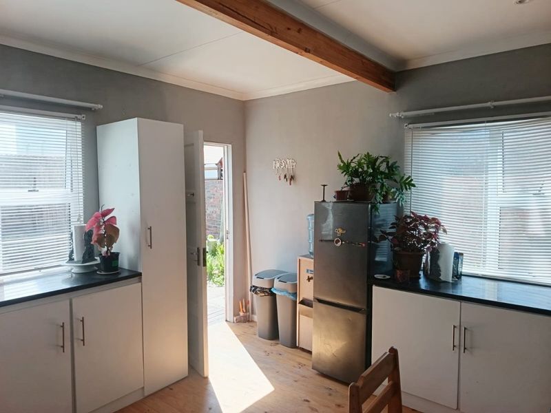 A functional kitchen area featuring white cabinetry, dark countertops, exposed timber ceiling beams, and direct access to the rear exterior.