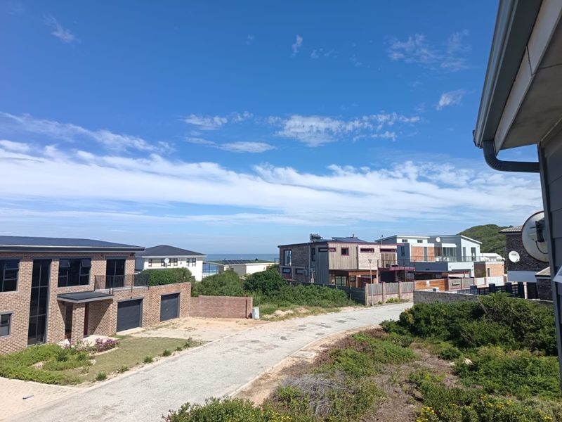 An elevated view overlooking a coastal residential neighbourhood with modern homes and a glimpse of the ocean in the distance.