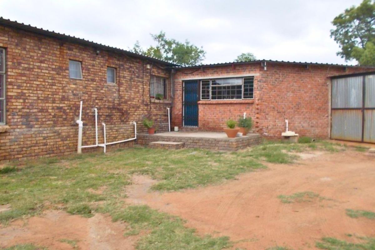 Rear view of a farm-style brick building featuring a raised patio, security gate, and corrugated metal roofing with visible external plumbing.
