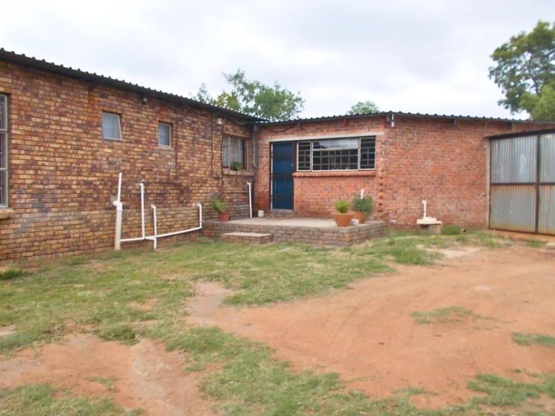 Rear view of a farm-style brick building featuring a raised patio, security gate, and corrugated metal roofing with visible external plumbing.