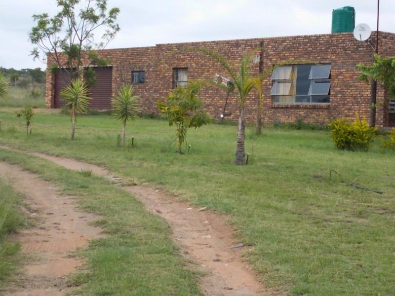 Front exterior view of a face brick farm building featuring a garage, top-hung windows, and an adjacent water storage tank on a rural property.