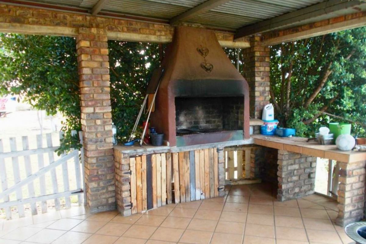 Covered outdoor patio area featuring a built-in brick braai, tiled flooring, and brick support pillars, ideal for outdoor entertaining.