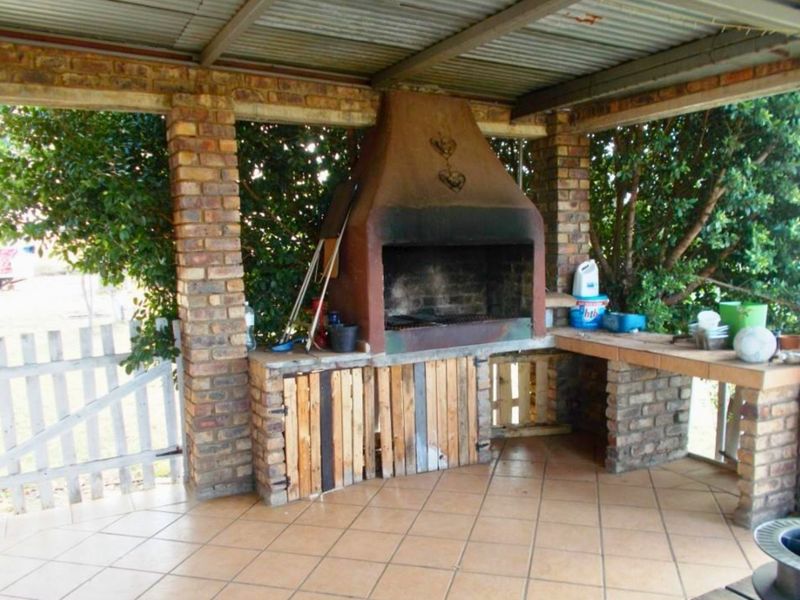 Covered outdoor patio area featuring a built-in brick braai, tiled flooring, and brick support pillars, ideal for outdoor entertaining.
