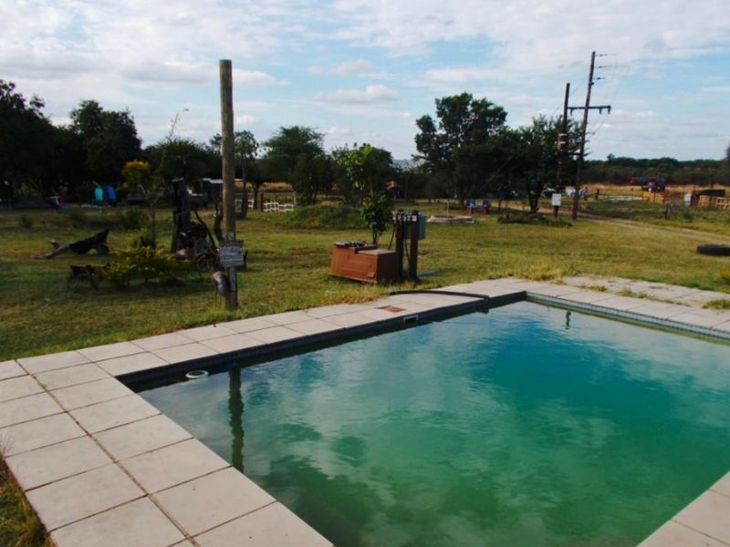 Outdoor swimming pool area set within a large farm garden, featuring tiled coping and adjacent pool pump infrastructure.