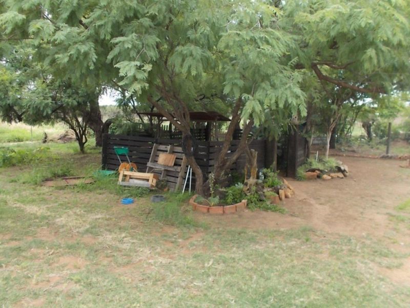 A rustic garden area on the farm featuring mature trees, timber fencing, and brick-edged garden beds in a natural, unmanicured setting.