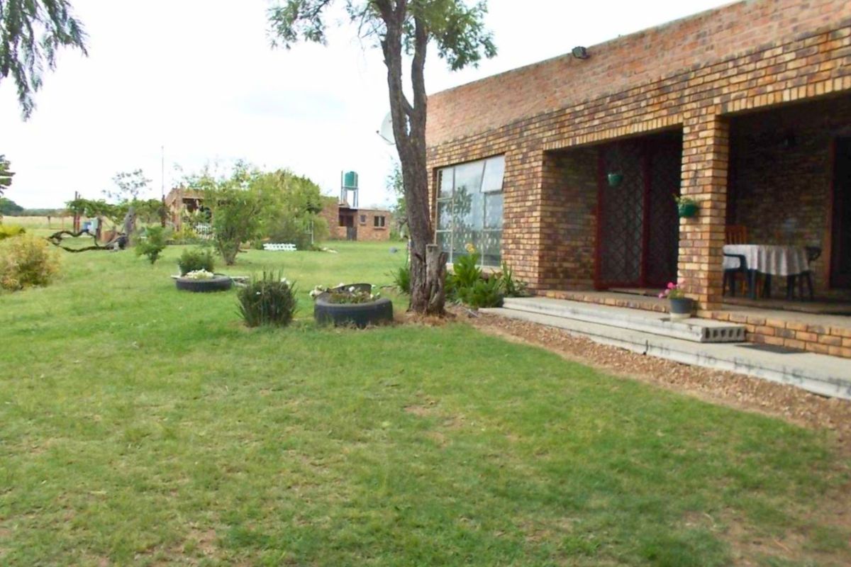 Rear view of a rustic brick farmhouse featuring a covered patio area and expansive lawn space.
