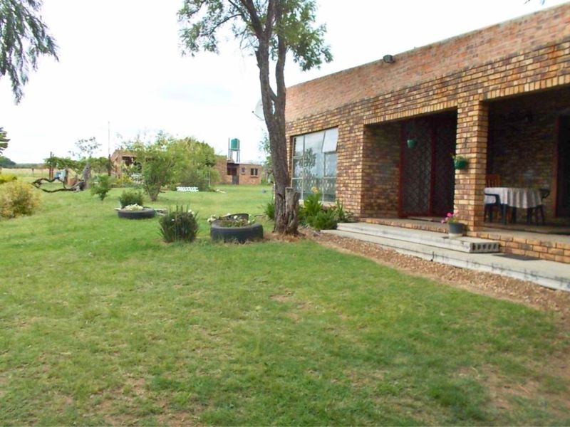 Rear view of a rustic brick farmhouse featuring a covered patio area and expansive lawn space.