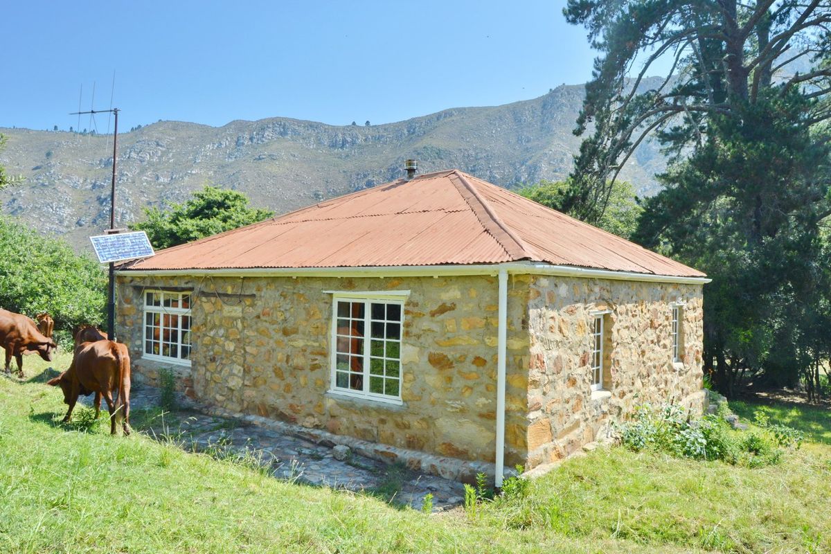 A rustic stone-walled farmhouse featuring a corrugated metal roof, solar panel installation, and scenic mountain views in a rural farm setting.