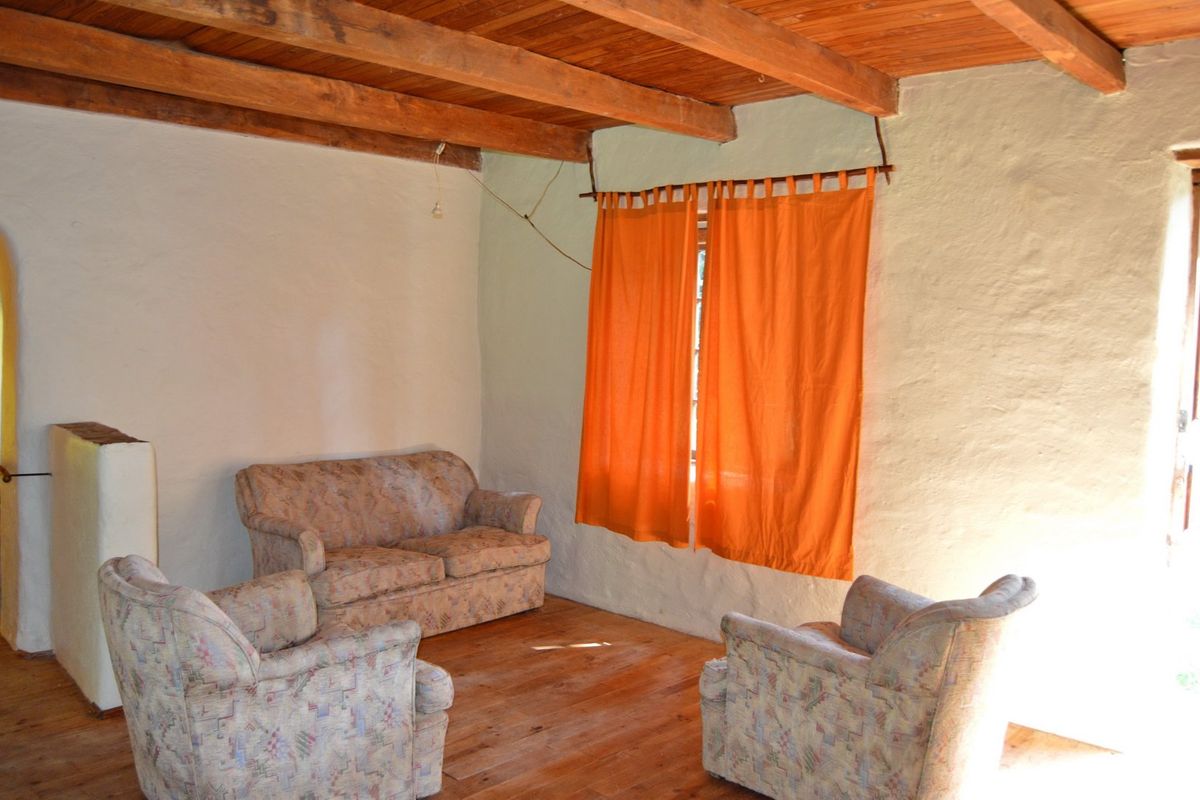 Rustic living room featuring exposed timber ceiling beams, textured plaster walls, and timber flooring, offering a traditional farm-style aesthetic.