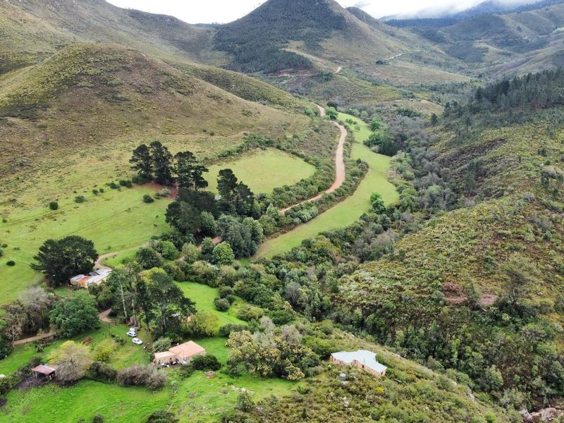 An aerial view of a rural farm property featuring rolling hills, natural vegetation, and a winding dirt access road.