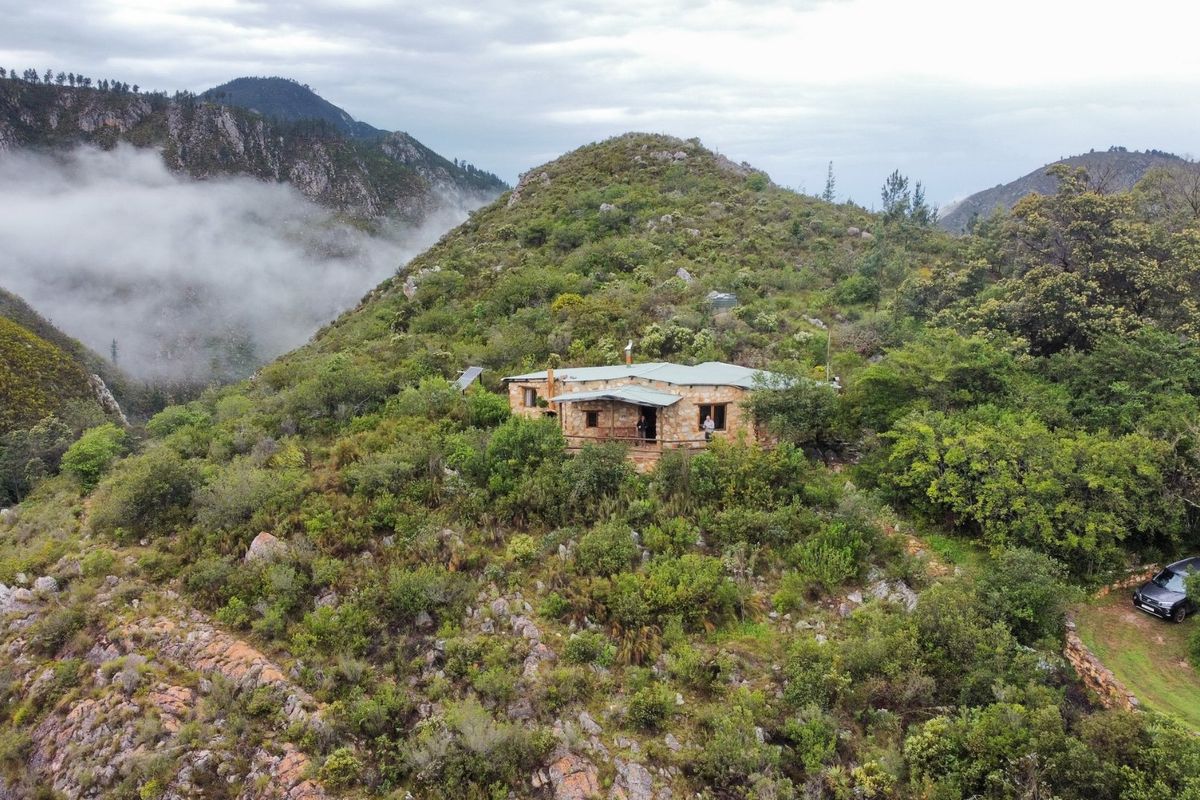 Aerial view of a stone-built farmhouse nestled in a scenic, mountainous landscape with lush vegetation and misty valley views.