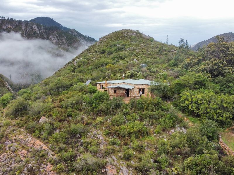 Aerial view of a stone-built farmhouse nestled in a scenic, mountainous landscape with lush vegetation and misty valley views.