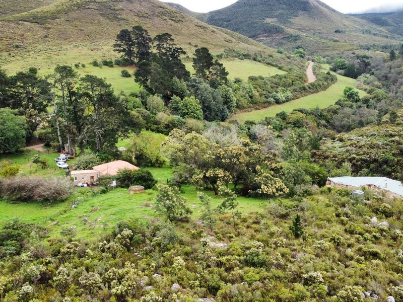 Aerial view of a rural farm property featuring multiple structures, natural landscape, and access roads set within a mountainous valley.
