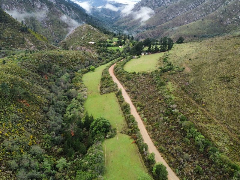 An aerial view of the farm property showcasing the expansive mountainous landscape, natural vegetation, and the access road winding through the pasture land.