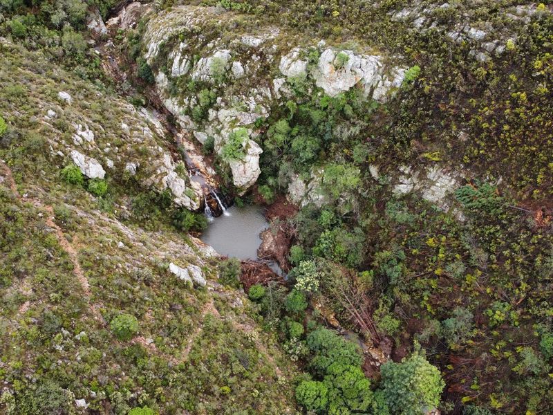 An aerial view of a natural waterfall cascading into a rocky pool, surrounded by indigenous vegetation and rugged terrain on the farm property.