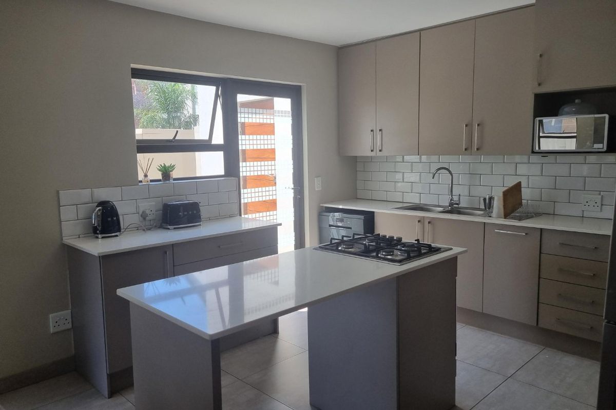 Modern kitchen featuring a central island with gas hob, quartz countertops, subway tile backsplash, and ample built-in cabinetry with direct access to the exterior.