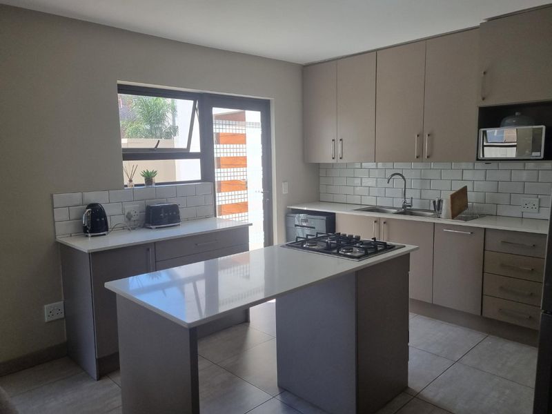 Modern kitchen featuring a central island with gas hob, quartz countertops, subway tile backsplash, and ample built-in cabinetry with direct access to the exterior.